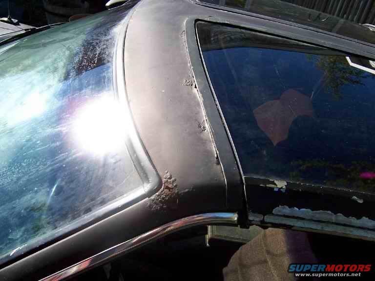 Close-up of a car's roofline showing rust on the trim near the windshield and side window