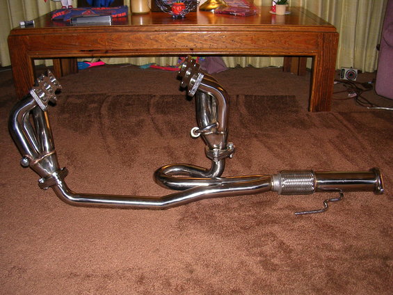 Chrome exhaust headers with a flexible pipe section, lying on a brown carpet