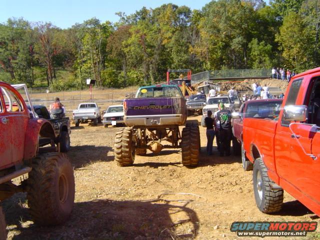 Several lifted trucks and buggies at a mud bogging event. A purple Chevrolet truck is in the center