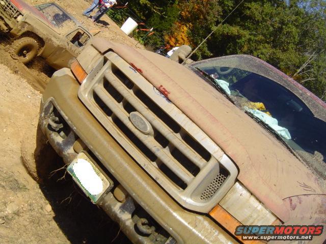 Mud-covered Ford truck grille, front view. Another muddy vehicle is visible behind