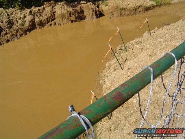 Green metal fence with wire mesh in front of a muddy pit with orange markers