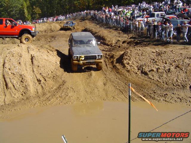 Gray 1979 Ford Bronco navigating a muddy obstacle course with spectators watching