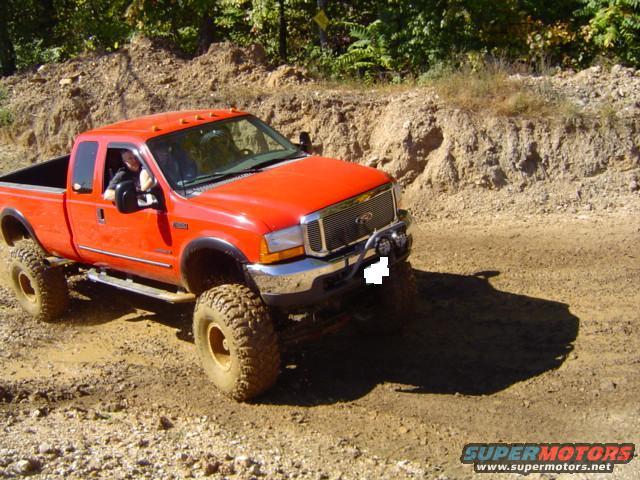 Orange Ford F-250 Super Duty pickup truck with large tires driving on a muddy dirt road