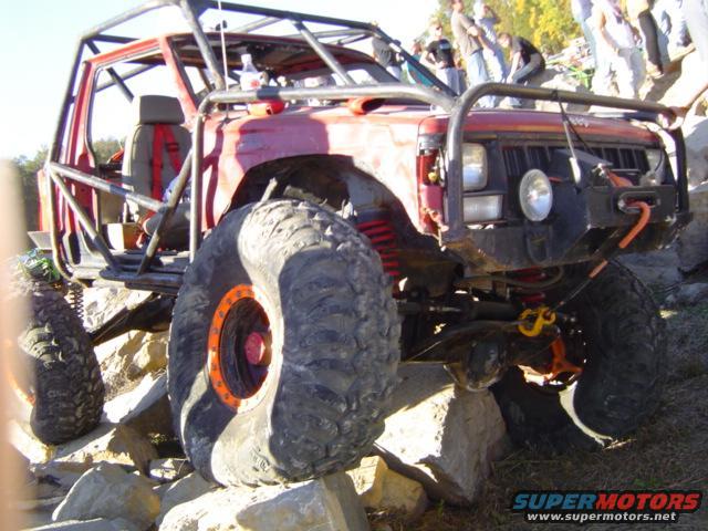 Red off-road vehicle with a full roll cage and large tires is on rocks