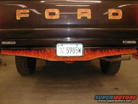 Rear of a dark Ford truck with flame decals on the bumper and tailgate. License plate reads 5985W
