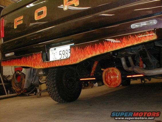 Rear of a dark-colored truck with flame decals on the bumper and tailgate. License plate reads 5989