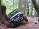 1990 Ford Bronco - A Jeep Wrangler navigates a steep, wooded trail, tilting precariously as it goes.