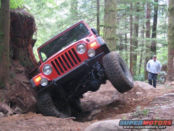 Red Jeep Wrangler tilted on a dirt trail with one wheel in the air