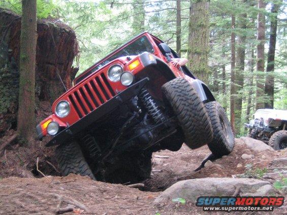 Red Jeep Wrangler tilted on rocky terrain, another vehicle in background