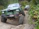 1990 Ford Bronco - A heavily modified green off-road vehicle tackles a challenging rocky terrain, with another vehicle visible in the background.