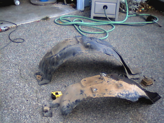 Two dirty plastic fender liners on a gravel surface