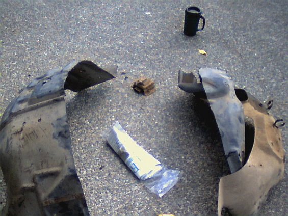 Two detached fender liners on asphalt, one with a plastic bag