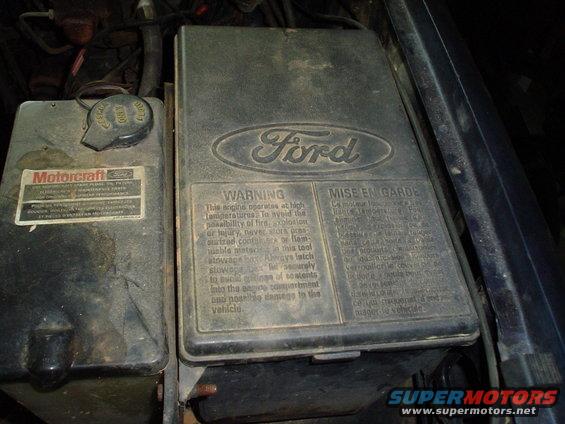 Ford engine compartment with Motorcraft fluid cap and warning label on a black box