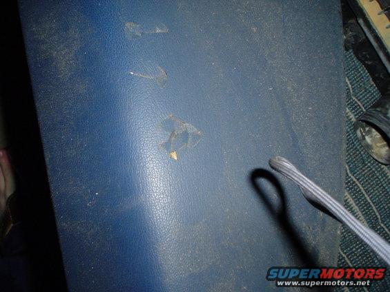 Close-up of a worn blue interior panel with several small tears and dust