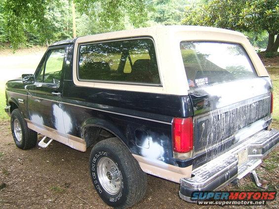 Black and tan Ford Bronco with body filler on the lower panels, viewed from the rear three-quarter angle