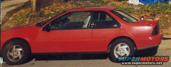 Red coupe with a spoiler, seen from the side. The car has a black trim and silver wheels