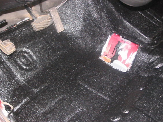 Vehicle floor with pedals and black spray-on bedliner. There's a red and white patch on the floor