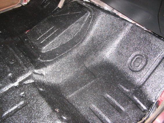 vehicle floor with textured black coating, showing molded contours and raised ribs