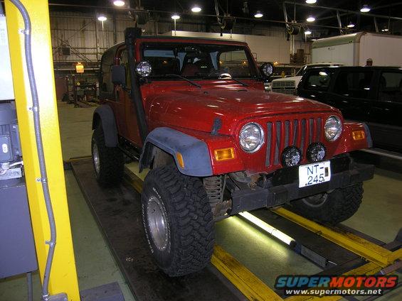 Red Jeep Wrangler on a lift, front view. Has a snorkel and aftermarket lights