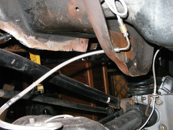 Underside of a vehicle showing rusty frame, suspension components, and brake lines