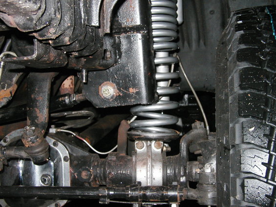 Close-up of a vehicle's front suspension with a coil spring, differential, and tire visible