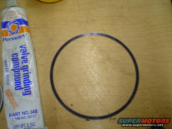 Permatex valve grinding compound tube next to a piston ring on a wooden surface