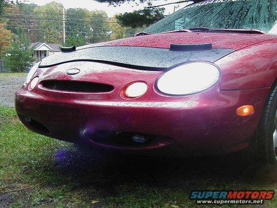 Red 1996 Ford Taurus front end with a black car bra, showing headlights, grille, and orange turn signals