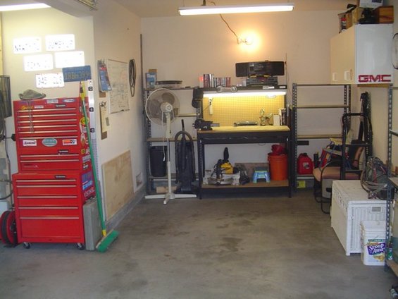 Garage with red tool chest, workbench, fan, and storage shelves