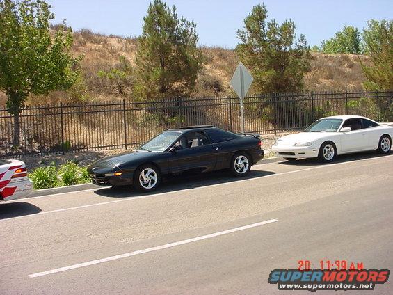Black Ford Probe parked on side of road, white car behind it