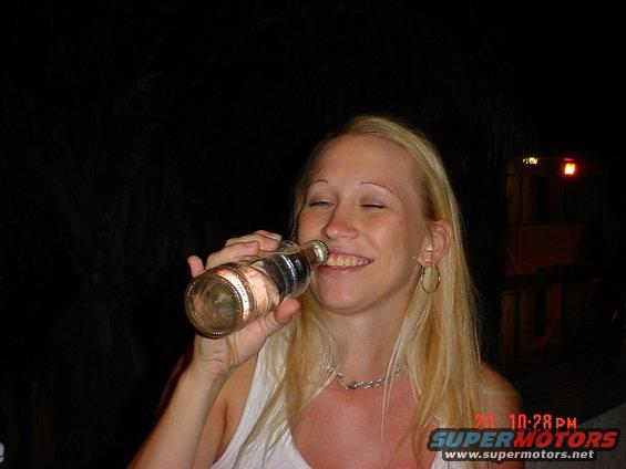 Woman drinking from a bottle at night, with a timestamp and website overlay