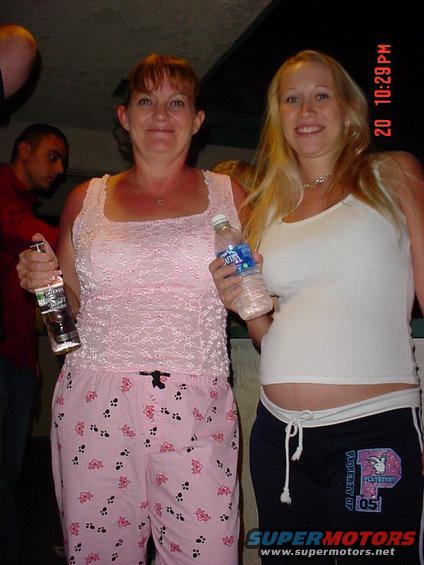 two women, one in pink pajamas, the other in a white tank top, holding drinks
