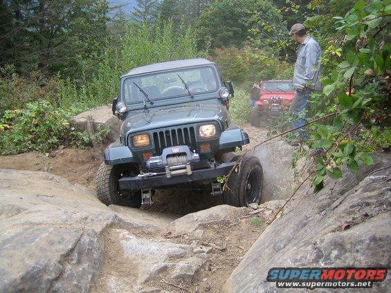 Gray Jeep Wrangler navigating rocky terrain, with a red Jeep in the background