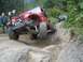 1990 Ford Bronco - A red Jeep Wrangler navigates a difficult rocky trail, with another Jeep visible further up the path.