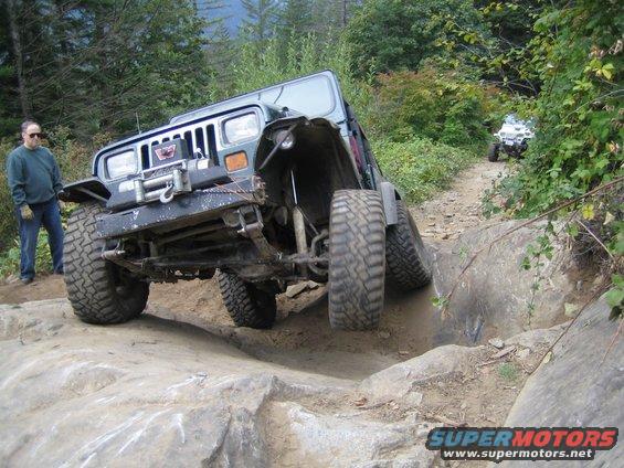Jeep Wrangler navigating a difficult rocky trail with a person standing nearby; another ATV is visible further down the path
