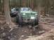 1990 Ford Bronco - Several off-road vehicles traverse a challenging, muddy path through a dense forest.