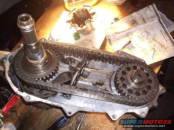 transfer case with chain and gears exposed, sitting on a wooden surface next to some diagrams