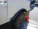 1987 Ford Bronco - Side view of a 1987 Ford Bronco's rear fender and tire, showing custom fender flares. A second vehicle is parked nearby.