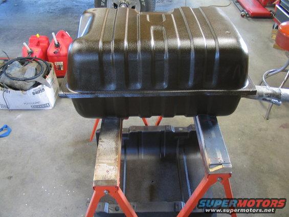 Brown fuel tank on orange jack stands, with red gas cans in background