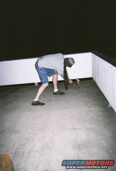 Person bending over to pick up a small figurine on a concrete surface