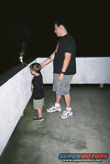 Dad holds a sparkler for his son to watch on a dark night