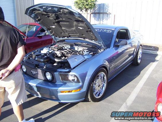 Blue Ford Mustang with hood open, chrome wheels, and a red car behind it