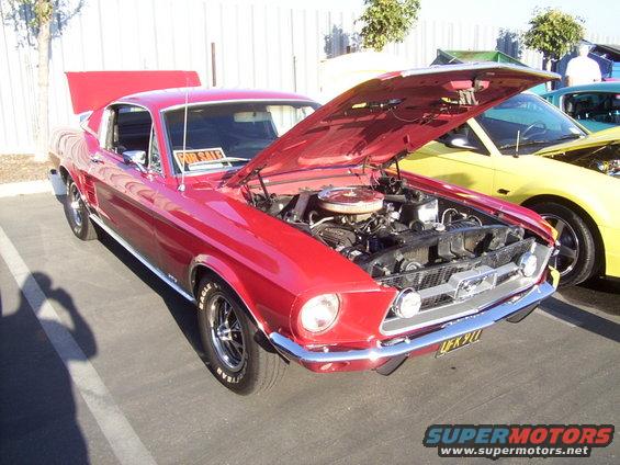 Red classic Mustang with hood open, parked next to a yellow car. 'For Sale' sign in window