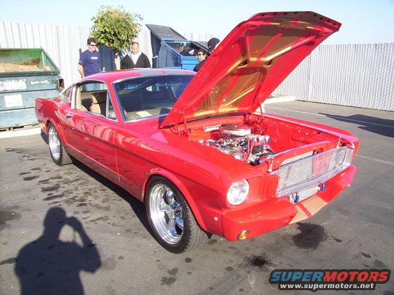 Red classic Ford Mustang, hood open showing engine. Chrome wheels, tan interior visible