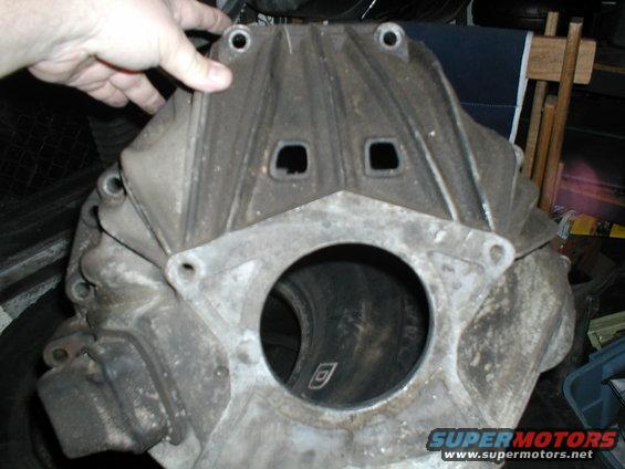 Dirty metal engine block with a large circular opening and two square holes above it. A hand is holding the top
