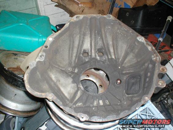 Used transmission bell housing, dusty and greasy, with mounting holes visible