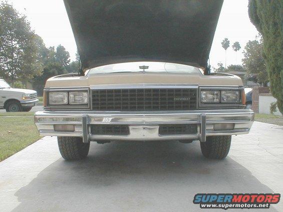 Front view of a tan 1977 Chevrolet Caprice with hood open. Another vehicle is parked to the left