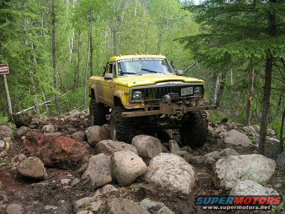 Yellow Jeep pickup truck with large tires on a rocky trail