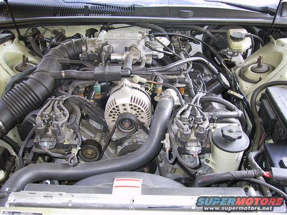 Engine bay with V8 engine components visible, including alternator, air intake, and spark plug wires