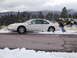1997 Ford Thunderbird - A white 1997 Ford Thunderbird is stuck in snow on the side of a road, with a person attempting to push it.