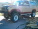 1985 Ford Bronco - A two-tone Ford Bronco is parked on a driveway with a trailer in the background.